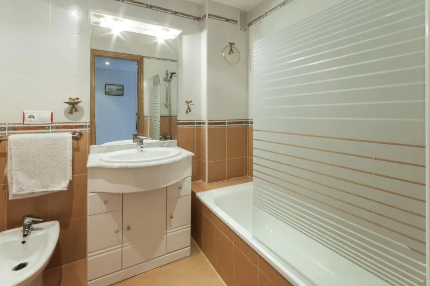 A bathroom with a sink, mirror, and bathtub behind a striped shower screen.