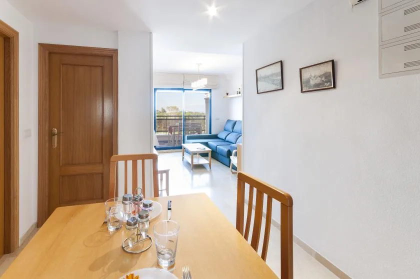 A dining area opens onto a bright living room with blue seating and a balcony.