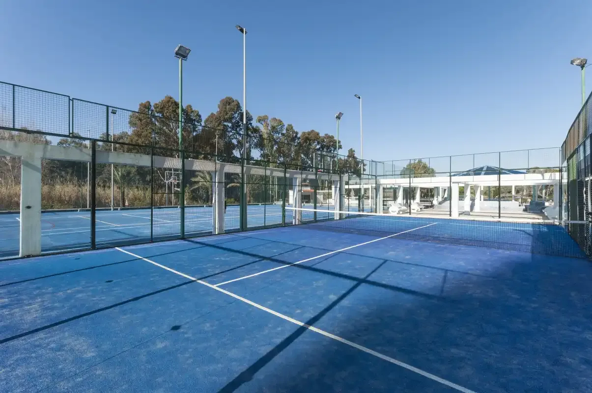 An outdoor sports court with blue playing surfaces, netting, and surrounding fencing.