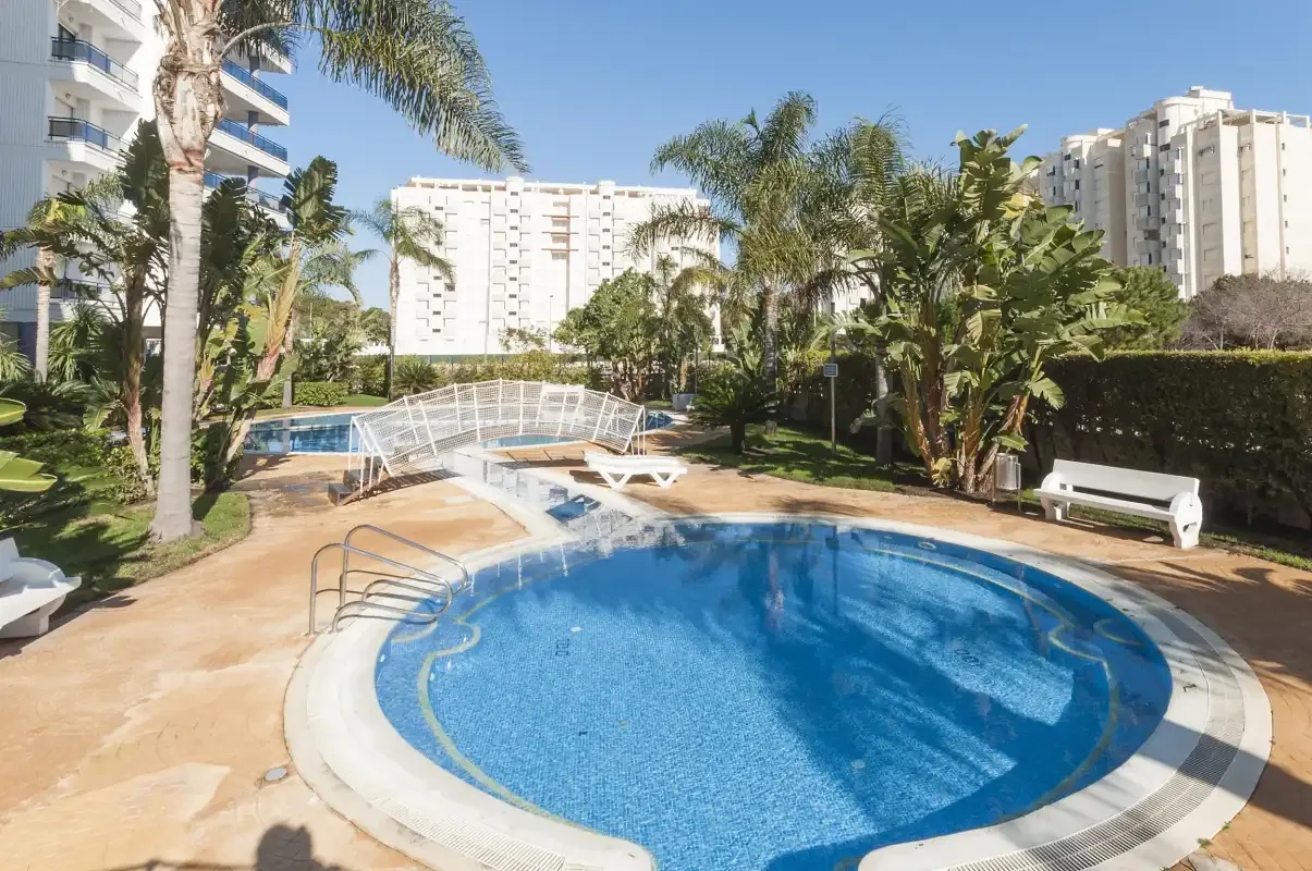 An outdoor swimming pool surrounded by palm trees and apartment buildings.