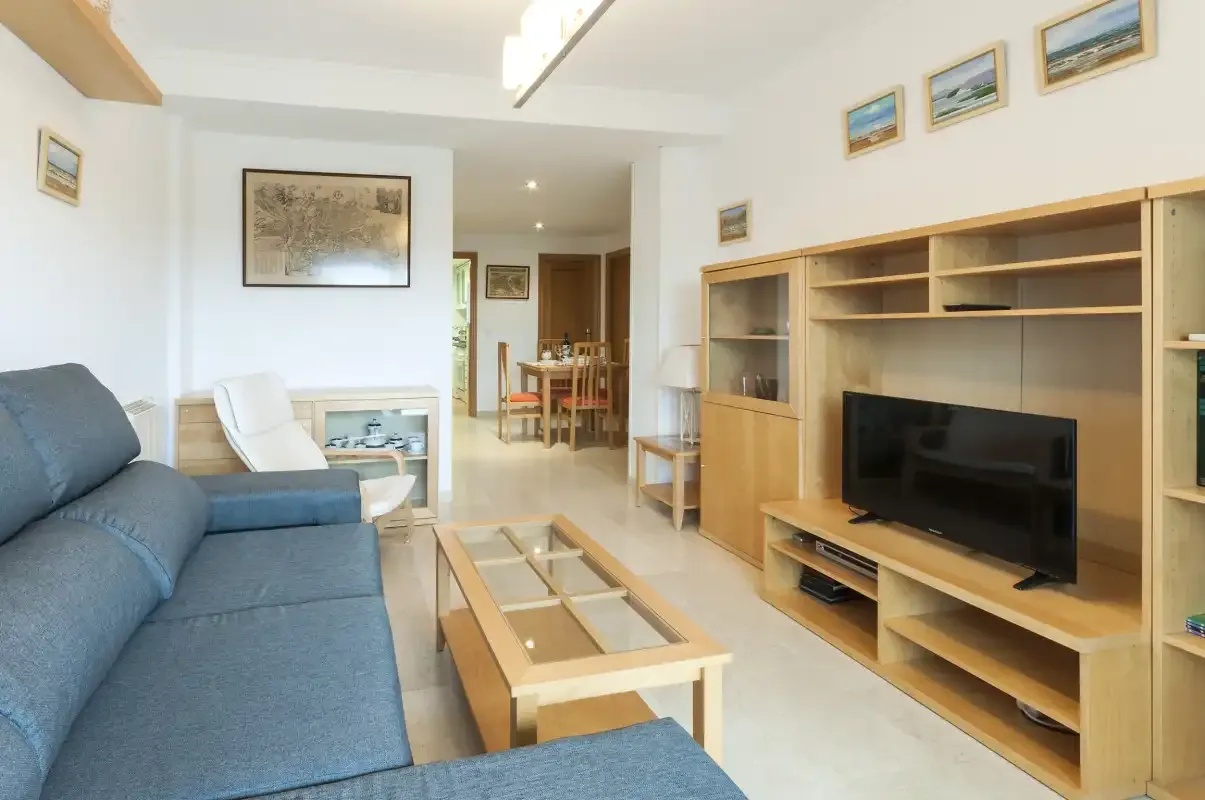 A living room with blue seating, a television, and a dining area beyond.