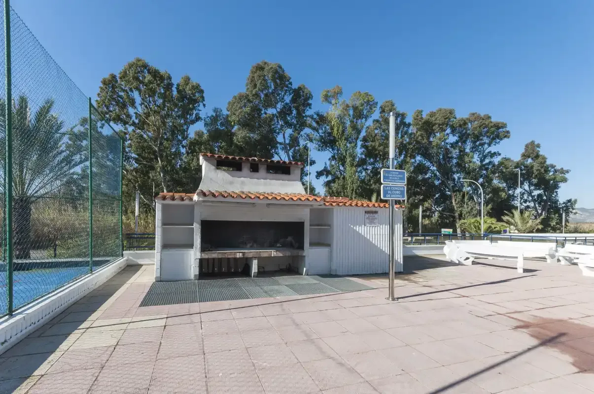 An outdoor recreation area with a fenced court, built-in grill, and paved patio.