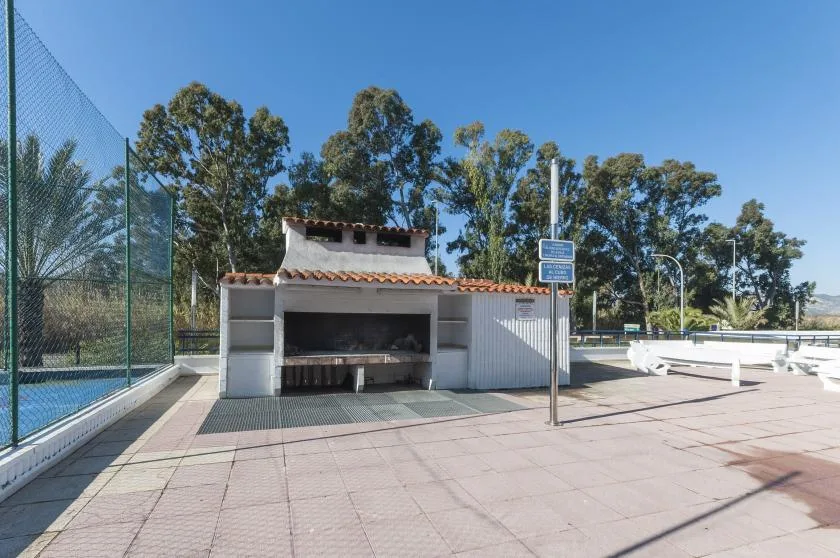 A paved outdoor recreation area with a fenced court and a covered barbecue station.