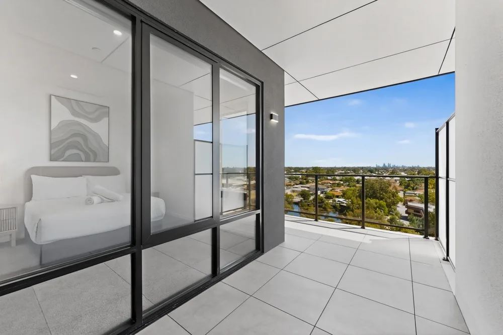 Dormitorio con una cama junto a un balcón con vistas a la ciudad.