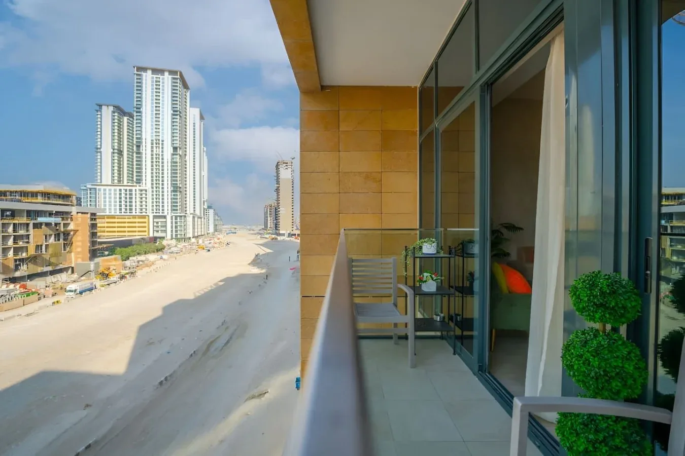 Un balcón con fachada de vidrio da a una playa de arena y edificios altos cercanos.