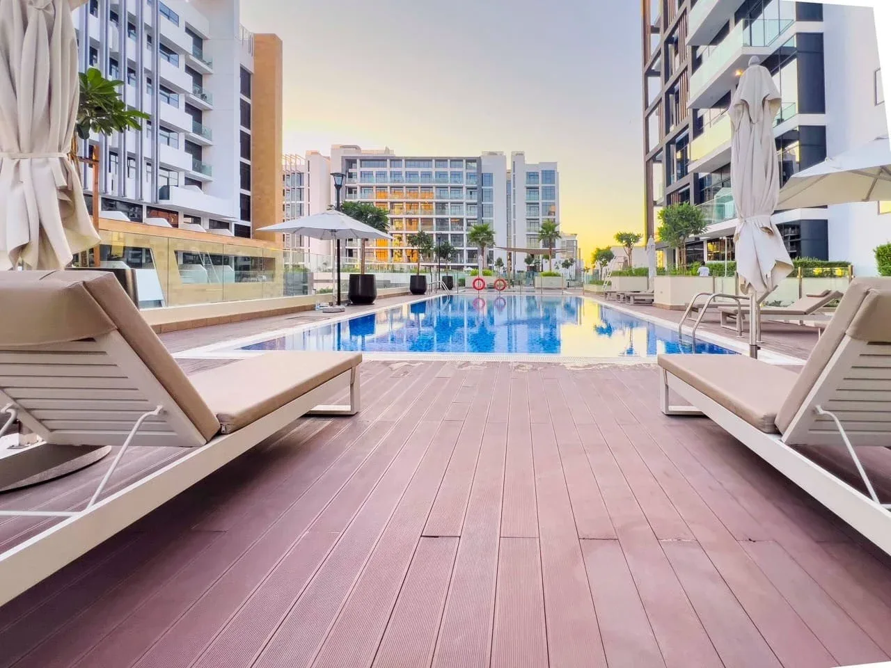Una piscina al aire libre está entre edificios modernos, con asientos de descanso junto a la terraza.