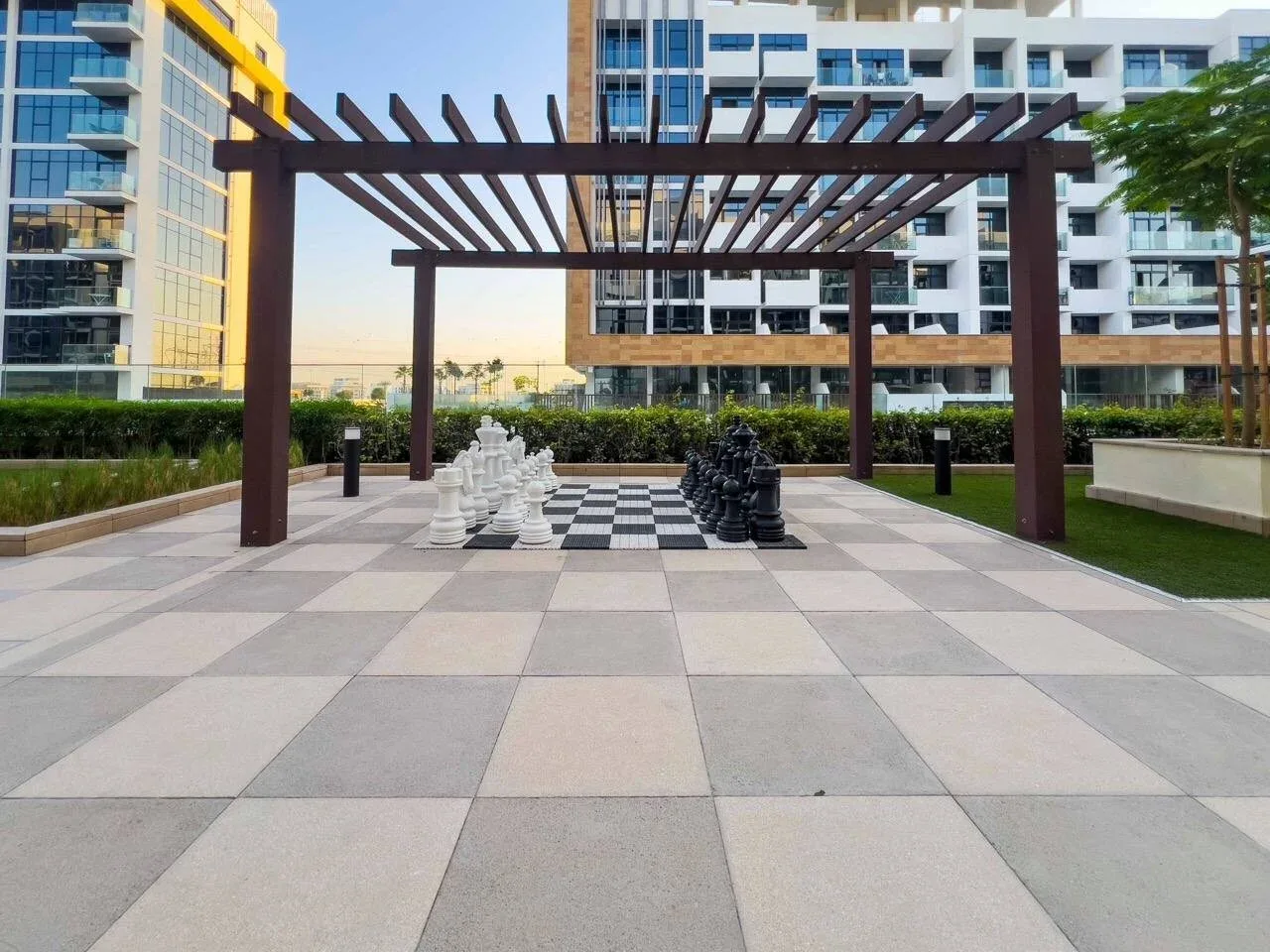 Una plaza al aire libre tiene un gran tablero de ajedrez bajo una pérgola de madera.