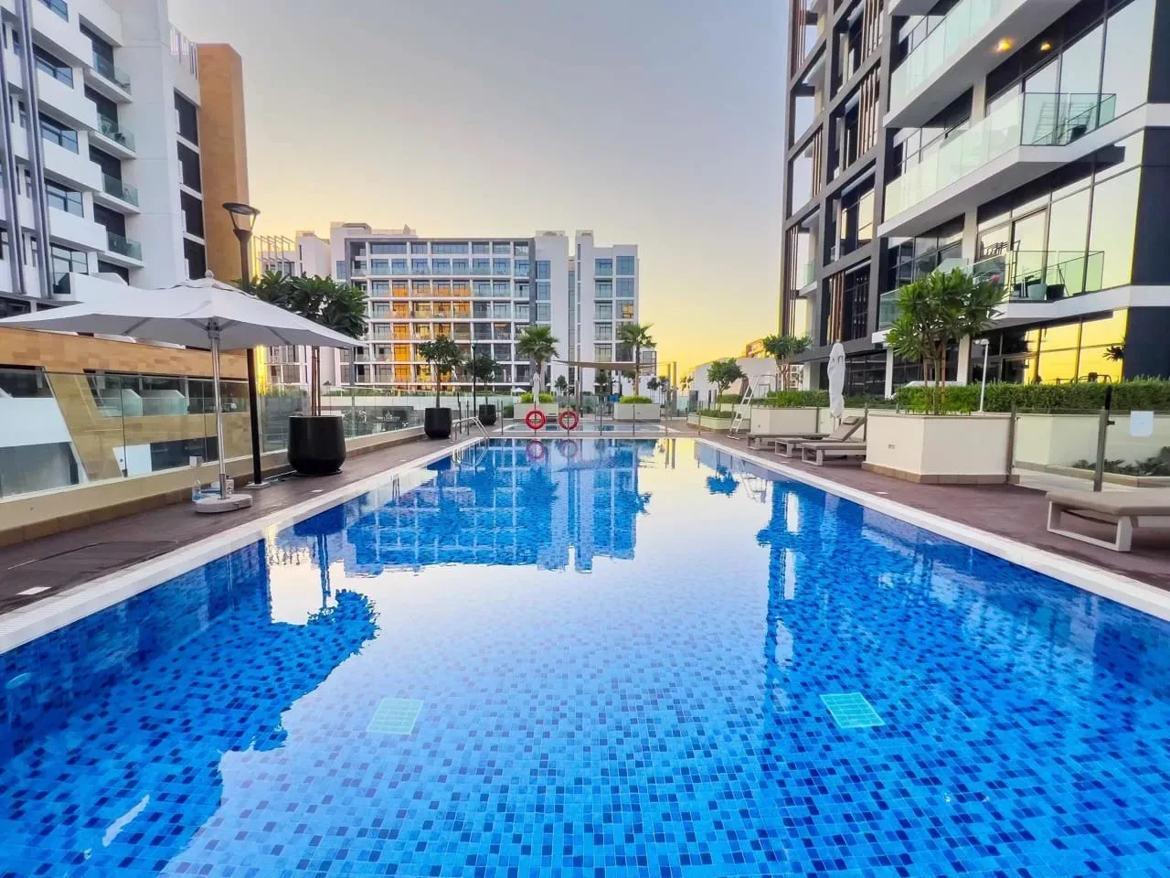 Una piscina al aire libre se encuentra entre edificios modernos al anochecer.