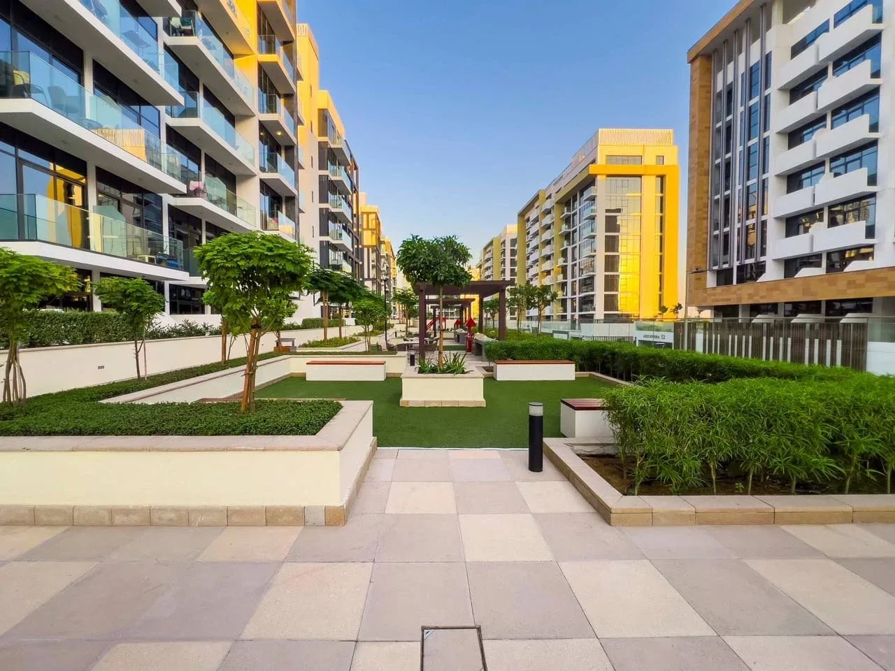 Patio ajardinado entre edificios de apartamentos modernos, con caminos pavimentados y jardineras.