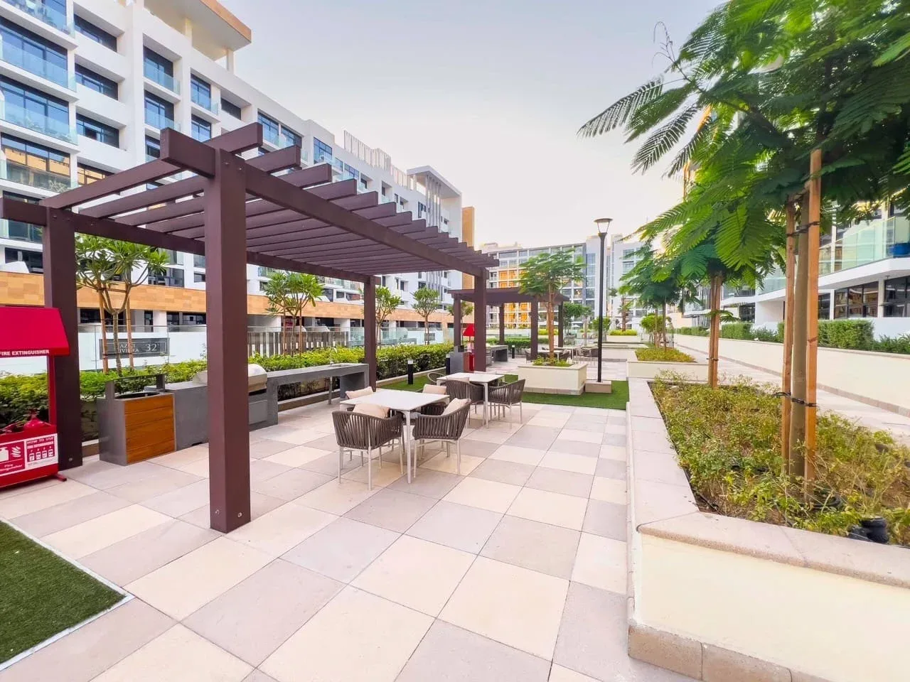 Un patio exterior con una pérgola sombreada, asientos y senderos ajardinados.