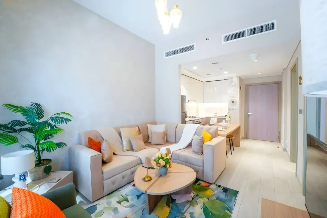 Una sala luminosa con una zona de asientos beige y una cocina abierta al fondo.