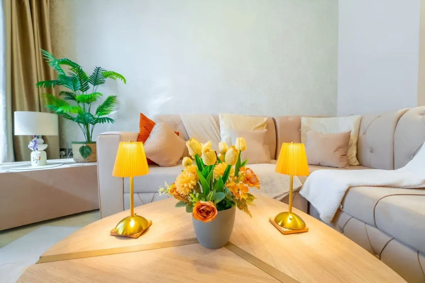 Una sala luminosa cuenta con un sofá seccional, una mesa de centro y flores amarillas.