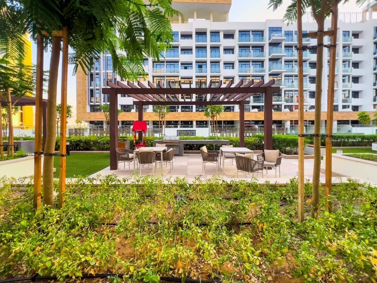 Un patio ajardinado tiene asientos al aire libre bajo una pérgola de madera.