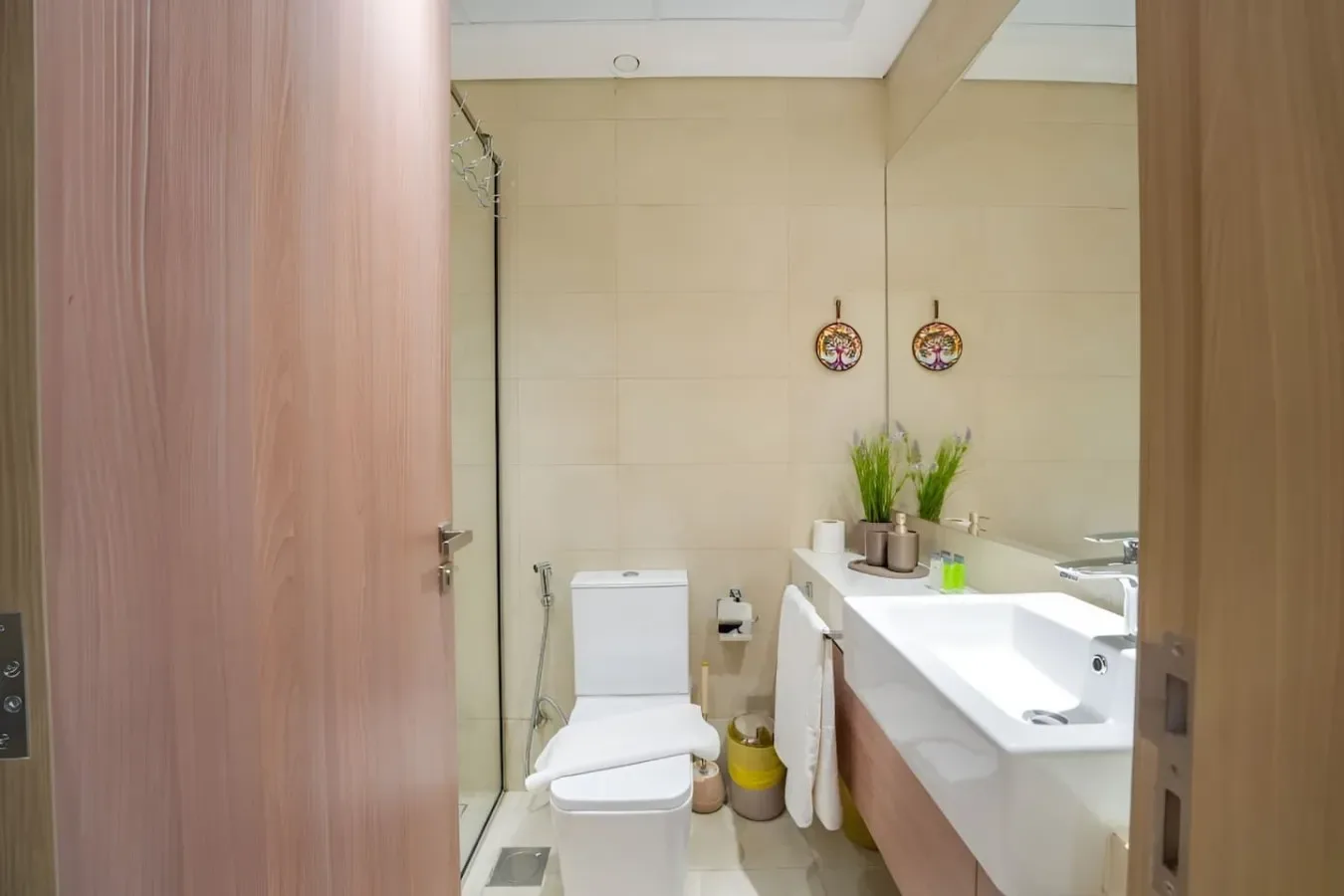 Un baño con azulejos, un inodoro, una encimera larga con lavabo y plantas en macetas.