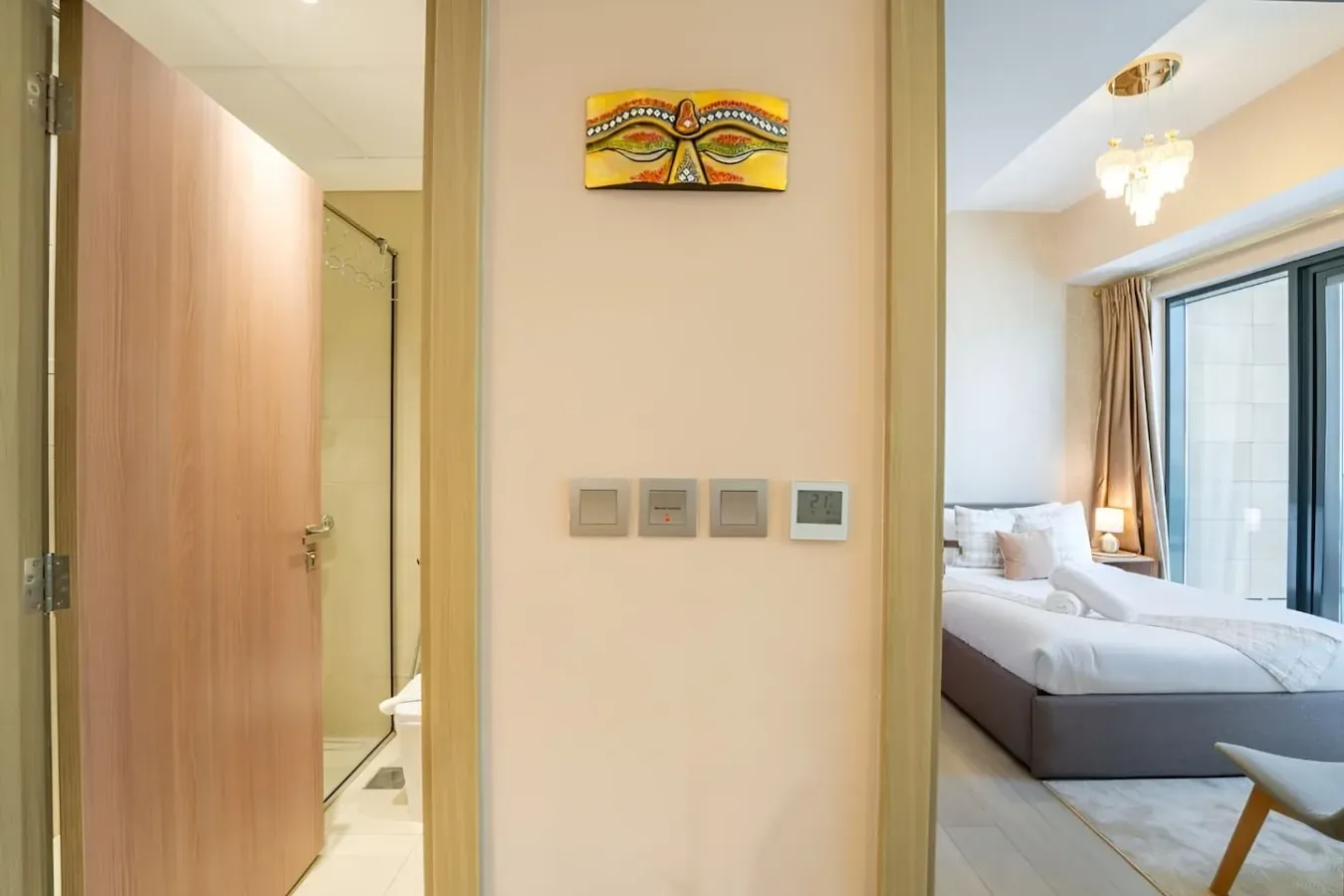 Un dormitorio con una cama junto a grandes ventanas, visible a través de una puerta abierta.