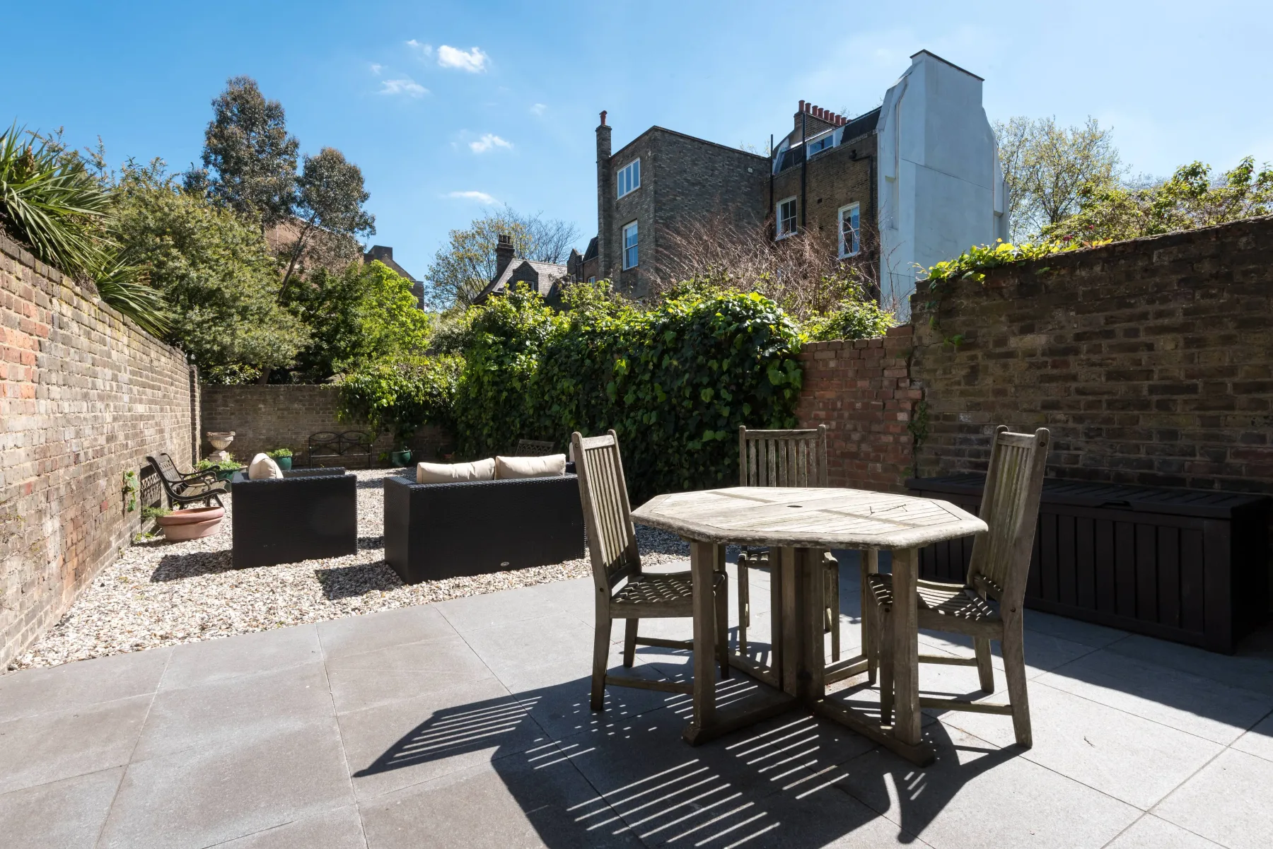 Un patio exterior pavimentado con una mesa de madera y asientos, rodeado de muros de ladrillo.