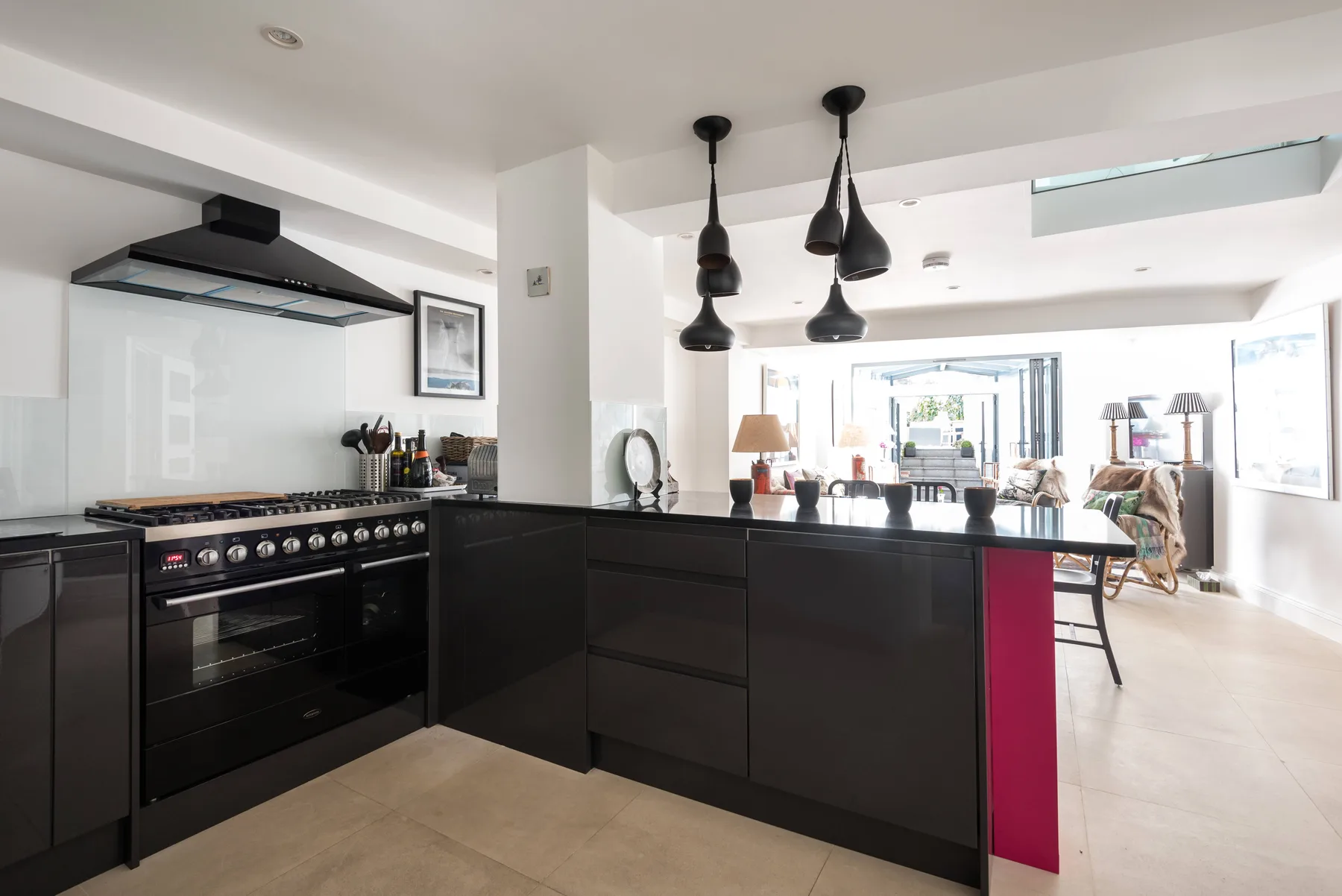Una cocina moderna con isla oscura y estufa se abre a una luminosa sala de estar.