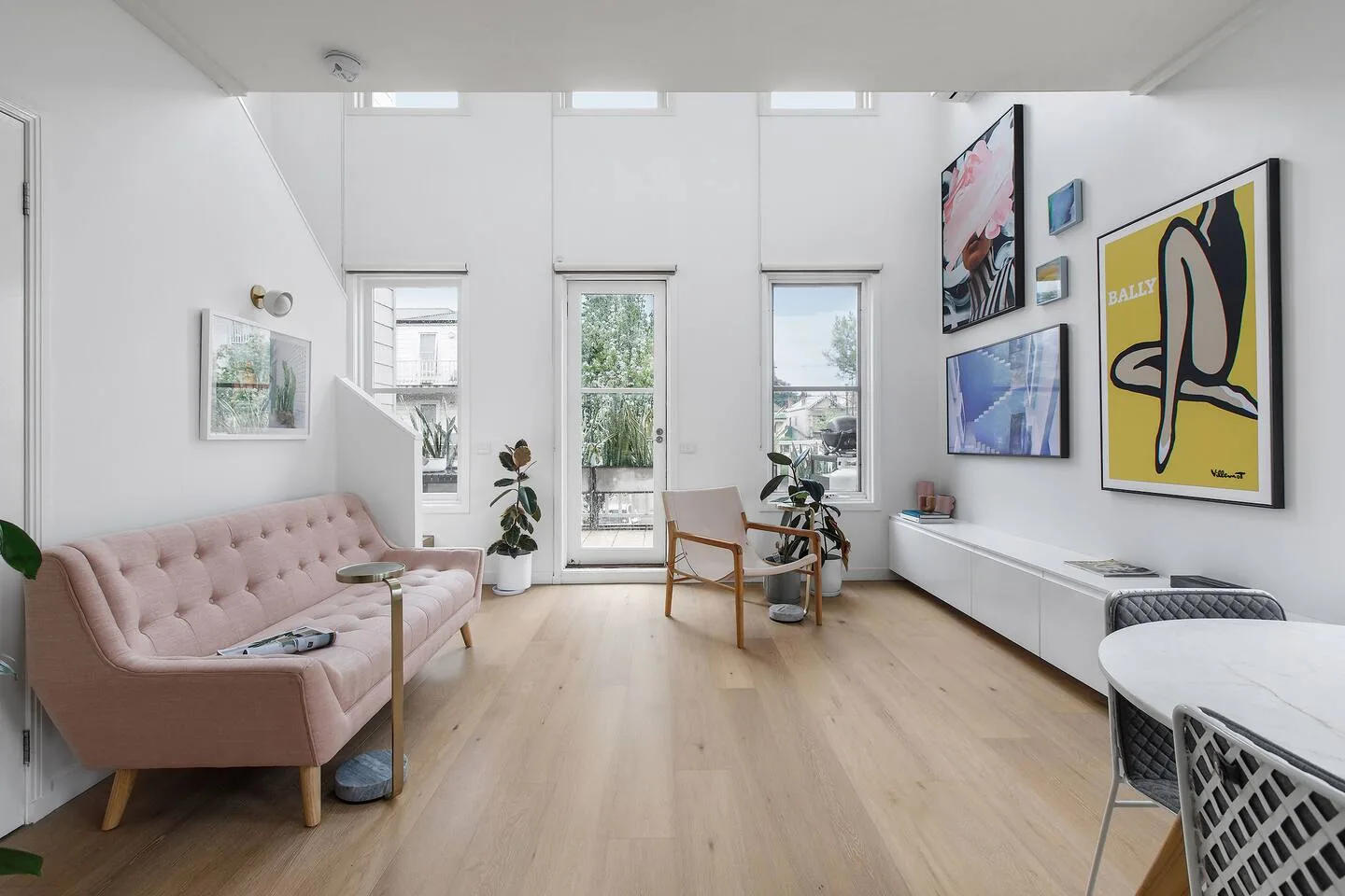Una luminosa sala de estar cuenta con un sofá rosa, obras de arte y ventanas altas.