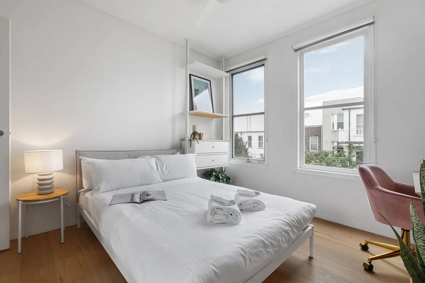 Un dormitorio luminoso con una cama, una lámpara de noche y una silla de escritorio junto a la ventana.
