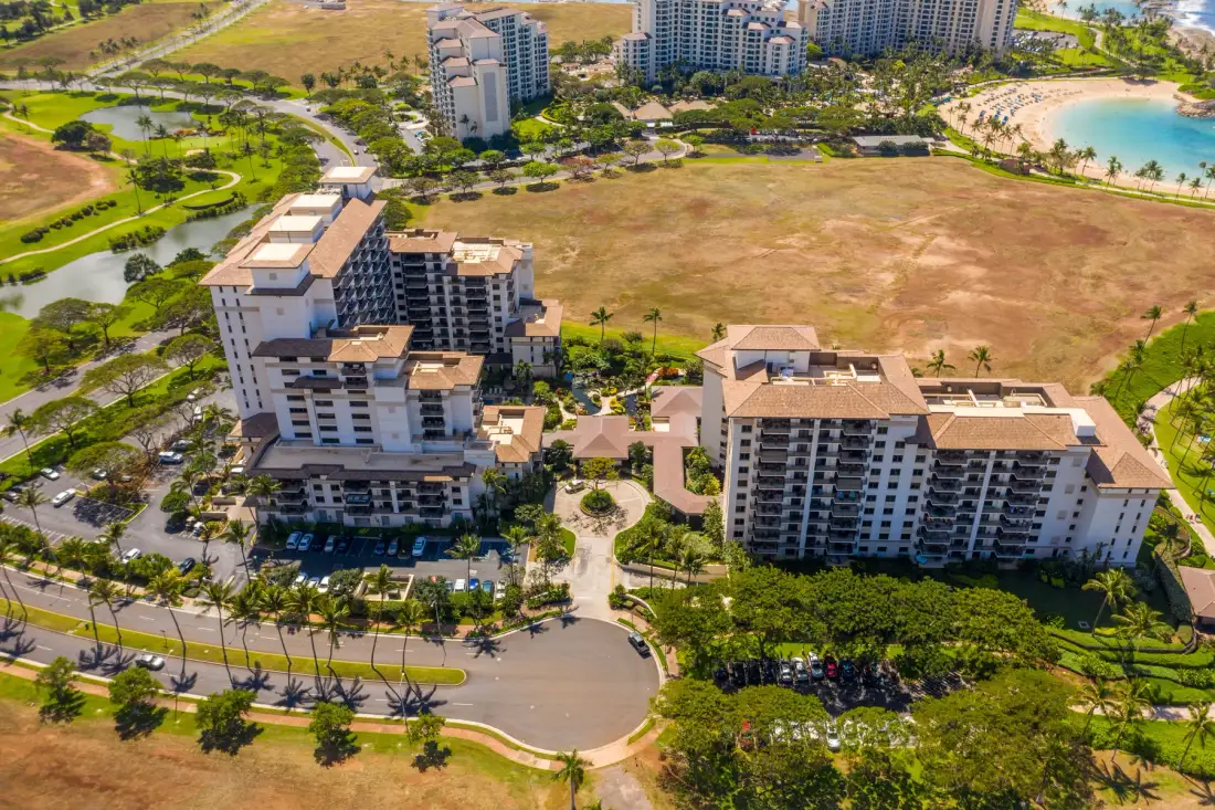 Vista aérea de edificios residenciales junto a una carretera ajardinada y una pequeña laguna.