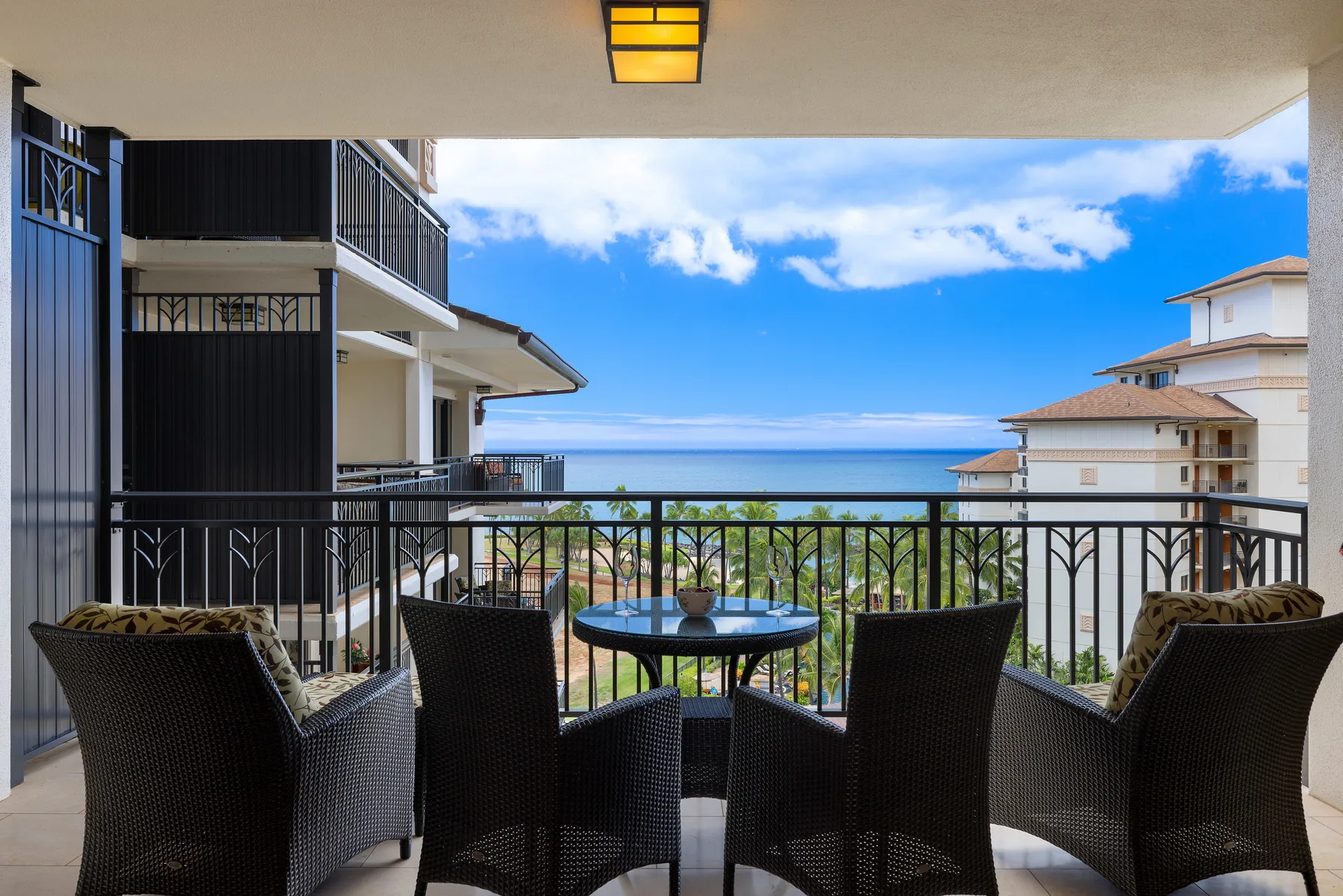 Un balcón cubierto tiene asientos de tejido oscuro alrededor de una mesa redonda y vistas al mar.