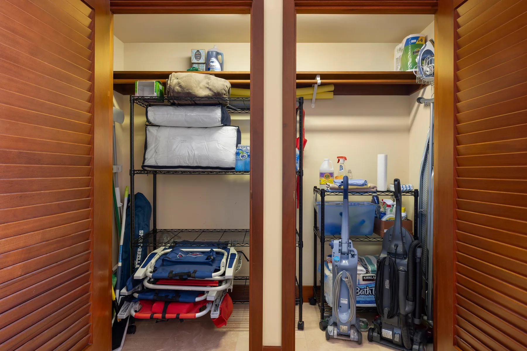 Dos armarios abiertos contienen ropa de cama apilada, artículos de limpieza y equipos.