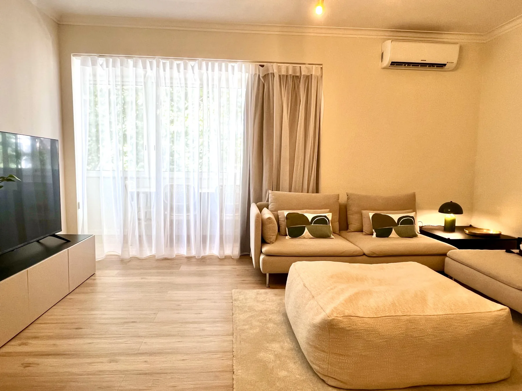 Una sala de estar con asientos, un televisor y cortinas sobre una ventana grande.
