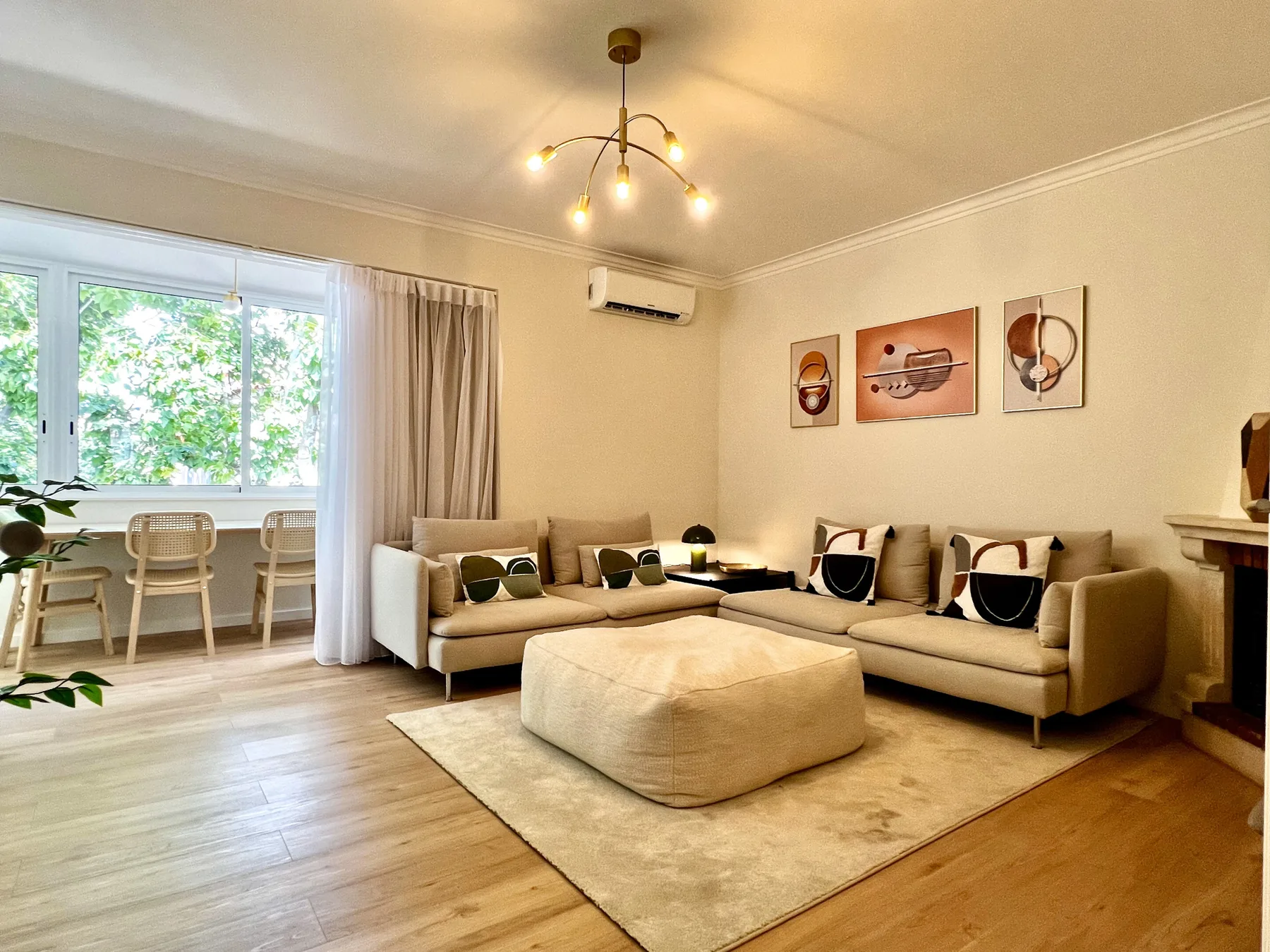 Una sala de estar luminosa con asientos alrededor de un otomano central y grandes ventanas.