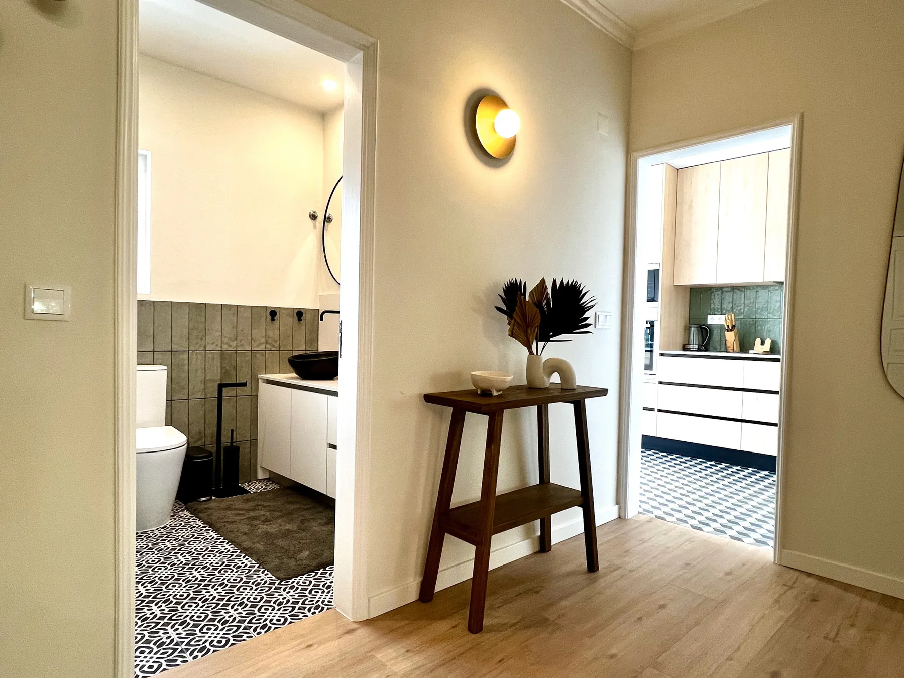 Un pasillo luminoso de apartamento tiene una mesa consola de madera entre dos puertas abiertas.