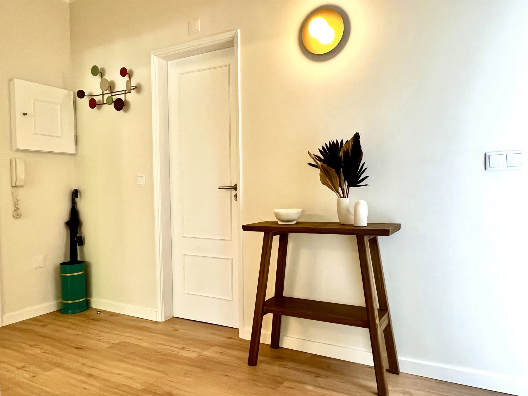 Una entrada luminosa cuenta con una consola de madera y un jarrón con ramas decorativas.