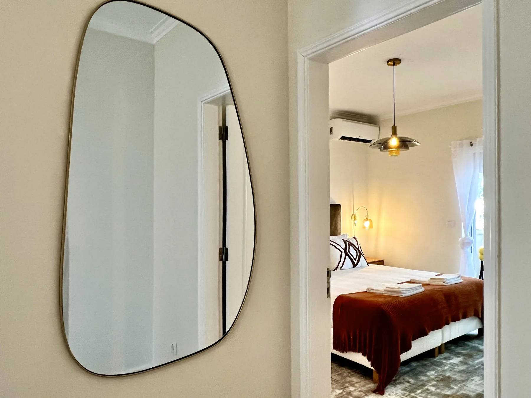 Se ve un dormitorio a través de una puerta, con una cama y una lámpara colgante.