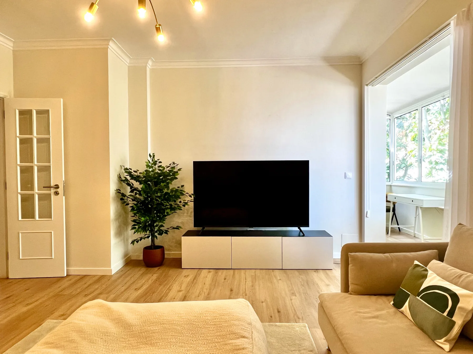 Una sala luminosa con televisor, asientos y una planta en maceta.