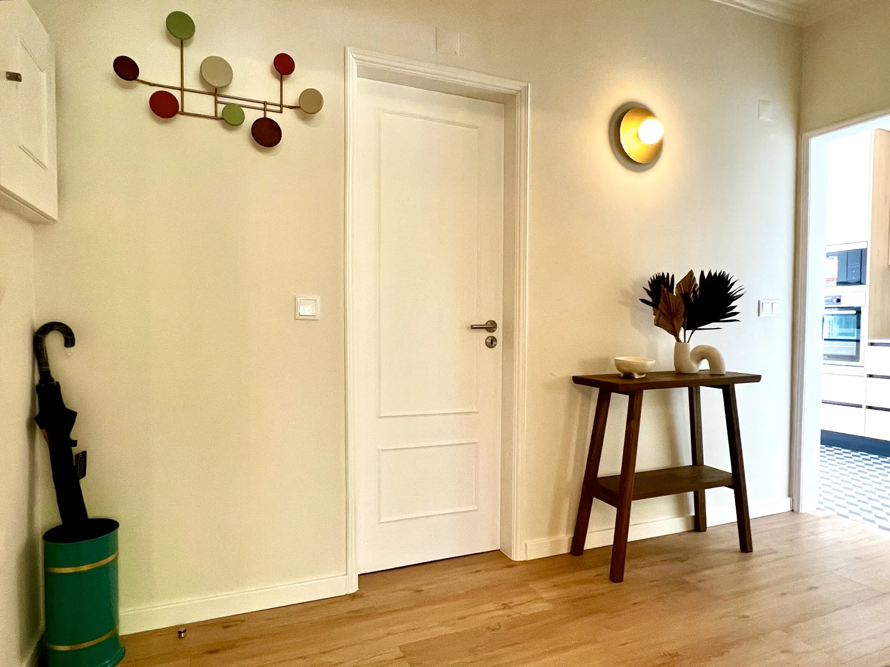 Una entrada con una puerta blanca, arte mural y una mesa estrecha de madera.