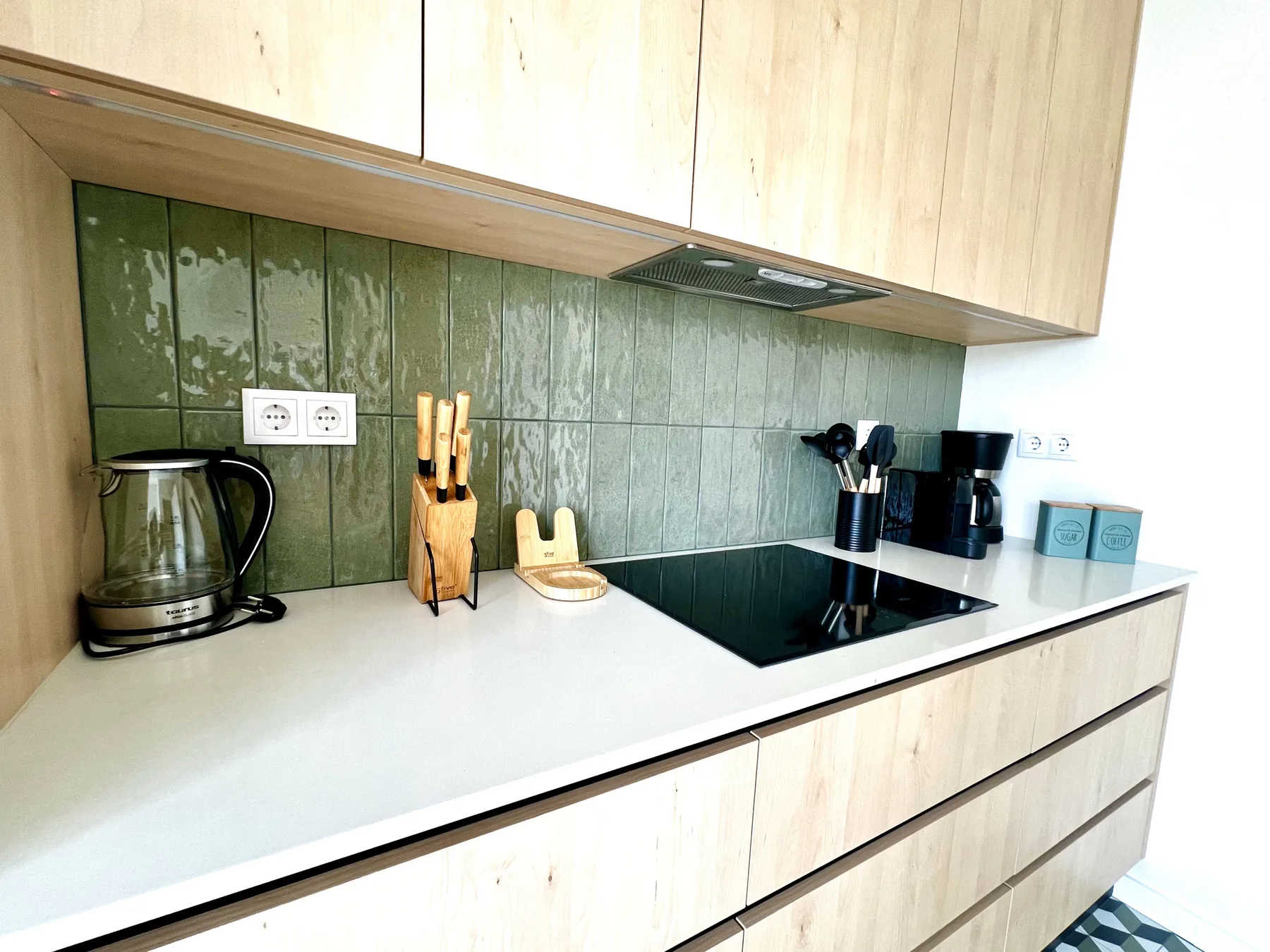 Una cocina moderna con una placa de cocción, un hervidor y una cafetera sobre la encimera.