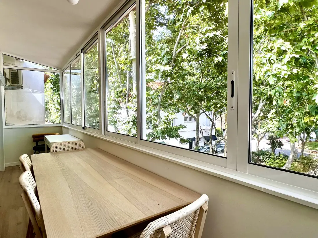 Comedor con una mesa larga junto a grandes ventanas con vistas a árboles frondosos.