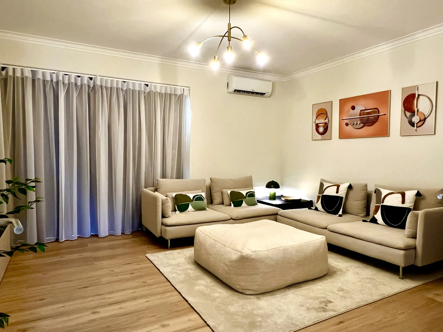 Una sala de estar con asientos en forma de L, mesa de centro y una gran ventana con cortinas.