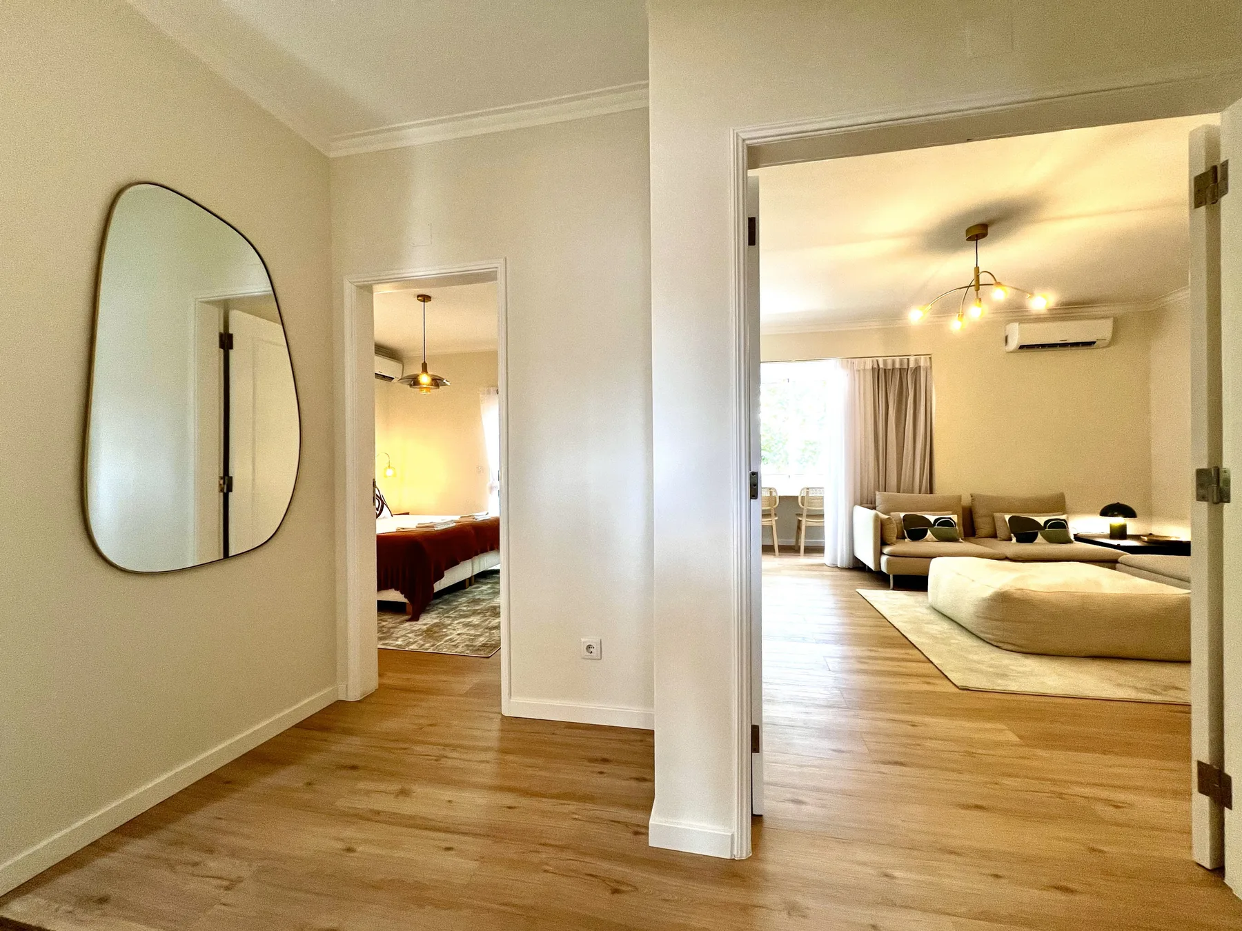 Un pasillo con un espejo de pared da a un dormitorio y una sala de estar.