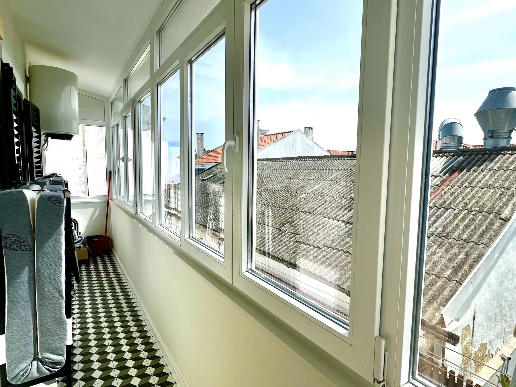 Un balcón estrecho y cerrado con grandes ventanas y suelo de baldosas estampadas.