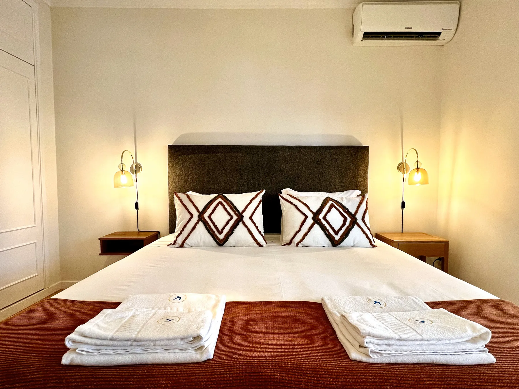 Un dormitorio con una cama, cojines estampados y luces de pared.