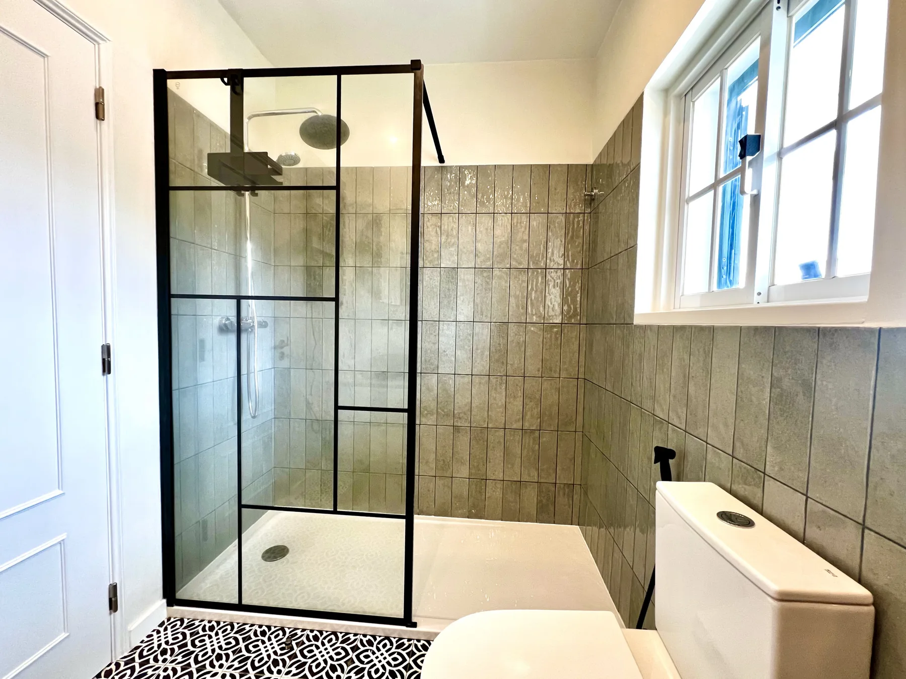 Un baño con azulejos, una ducha de cristal y una ventana.
