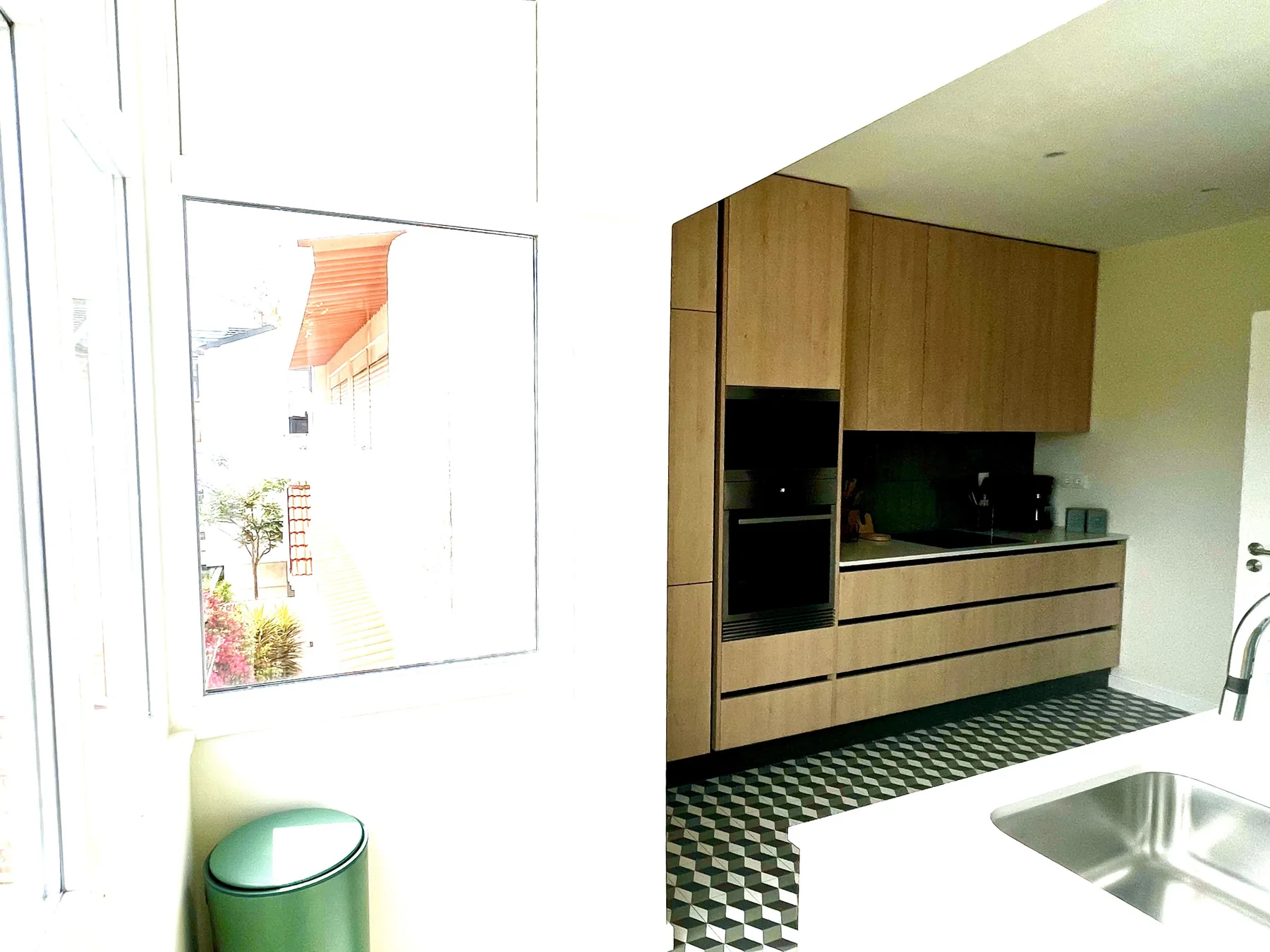 Una cocina moderna con gabinetes de madera, electrodomésticos oscuros y suelo estampado.