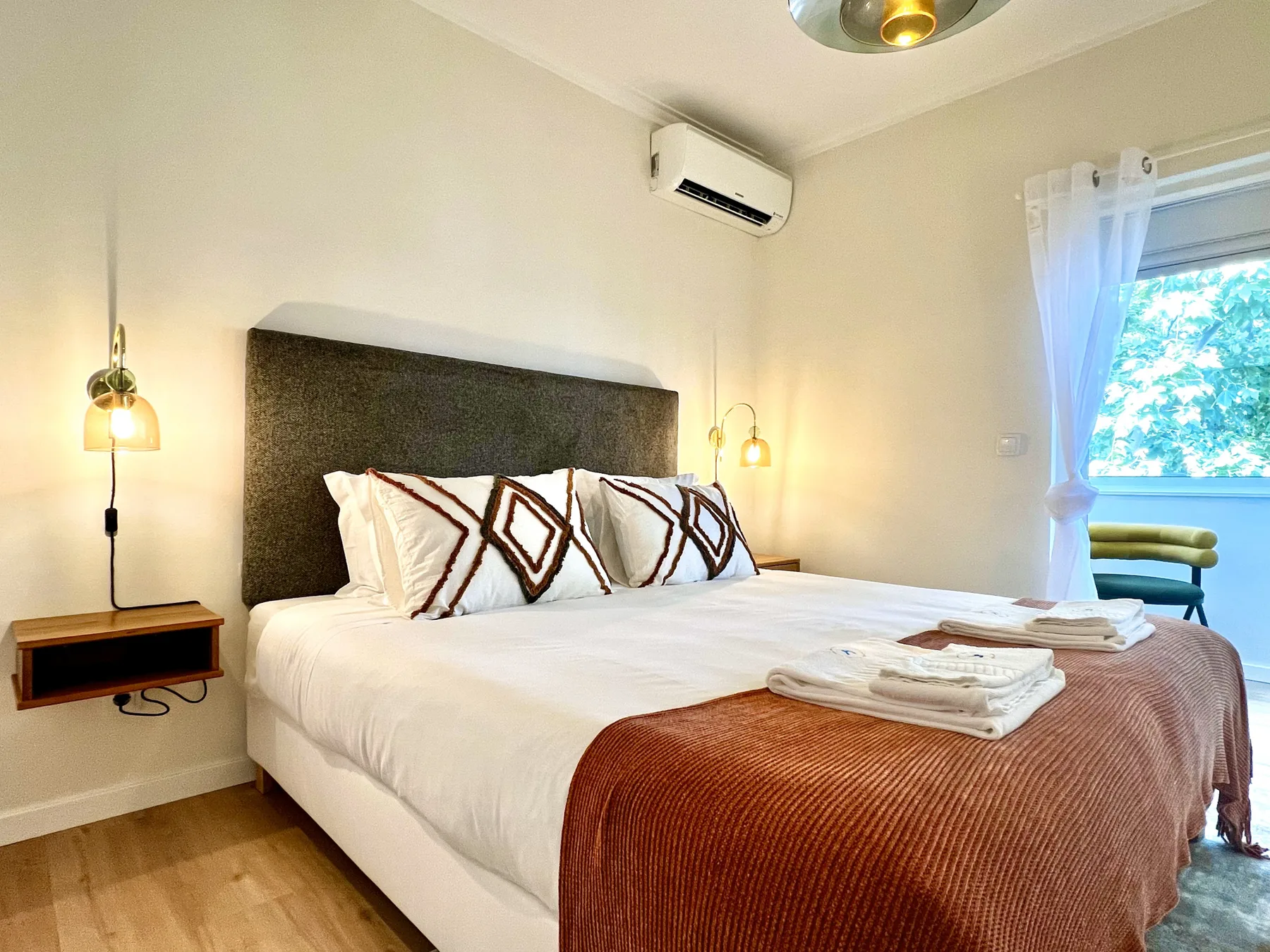 Un dormitorio con una cama bien tendida y almohadas estampadas junto a una ventana.