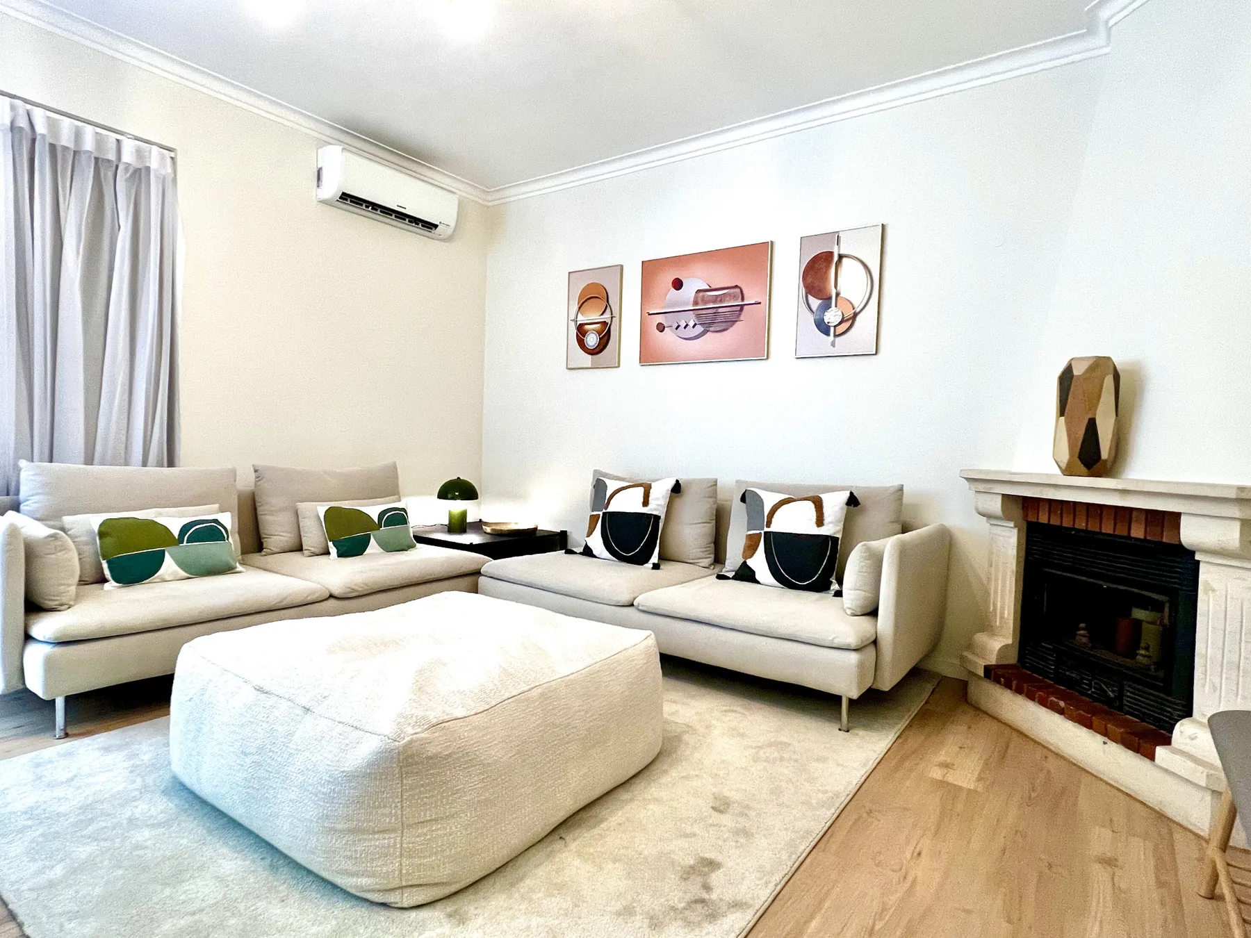 Una sala luminosa tiene asientos seccionales, un otomano grande y una chimenea.