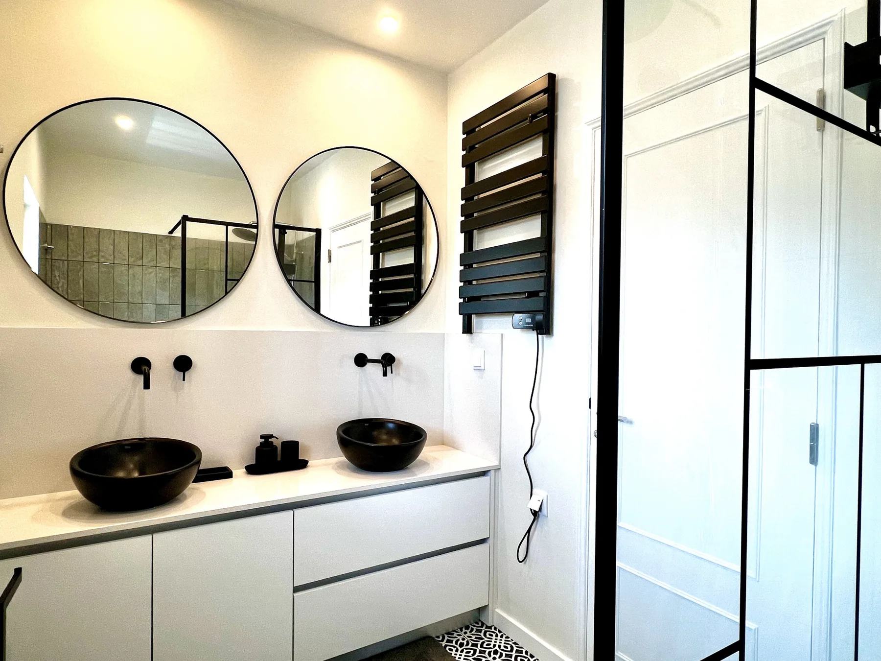 Un baño luminoso con un mueble de doble lavabo y espejos redondos.