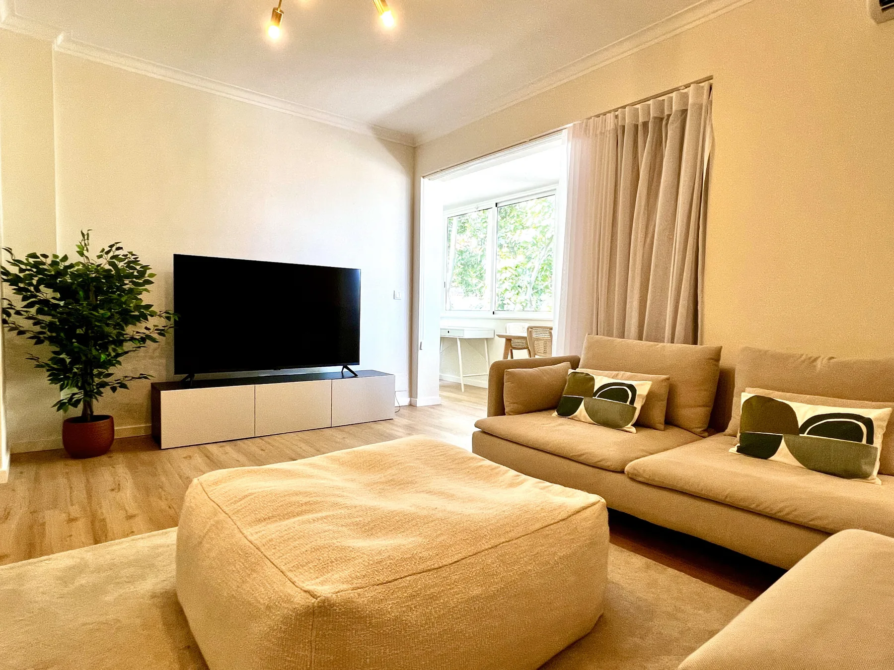Una sala luminosa con asientos, un televisor y un gran puf tapizado.
