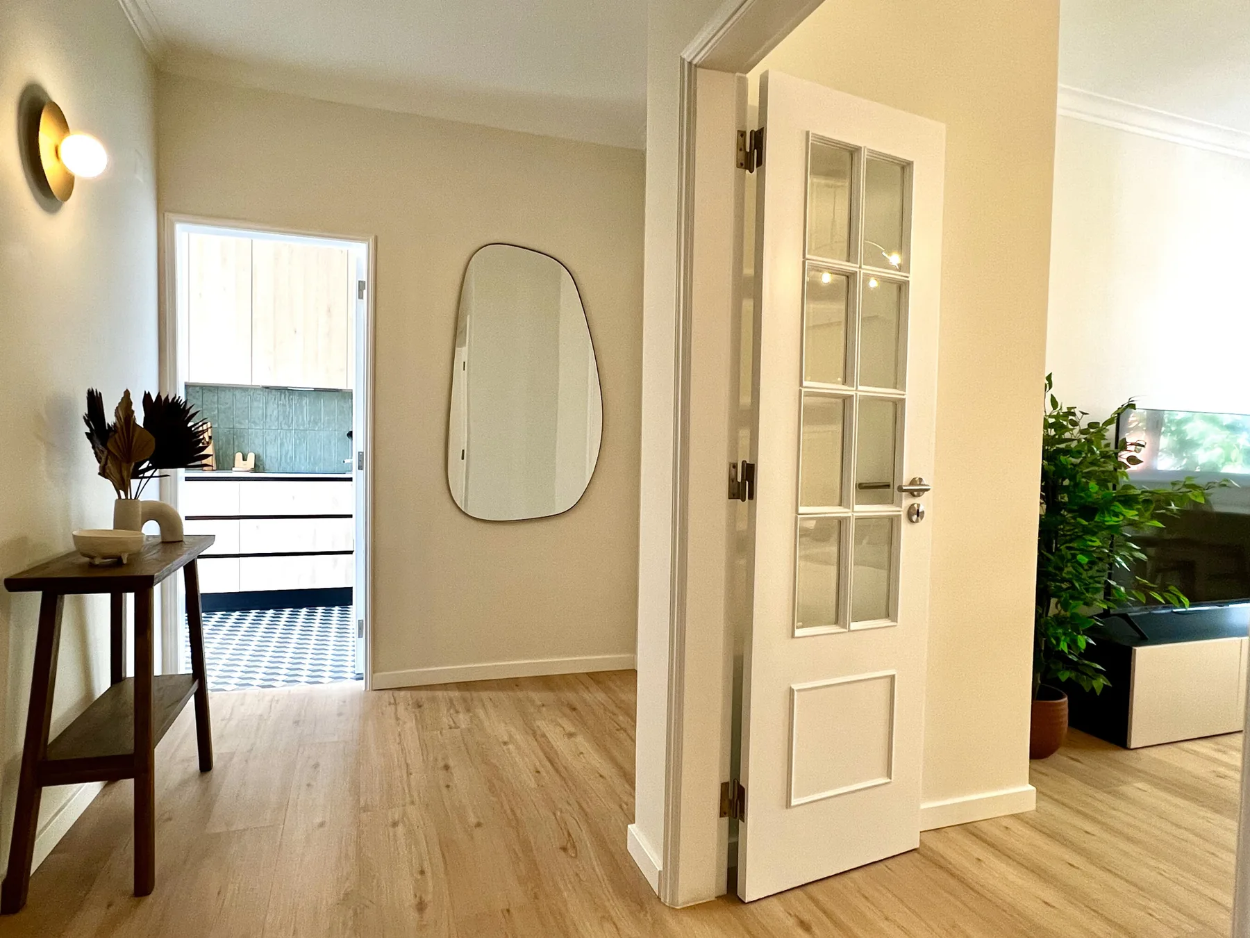 Entrada de un apartamento con un espejo, una puerta abierta y una pequeña mesa consola.