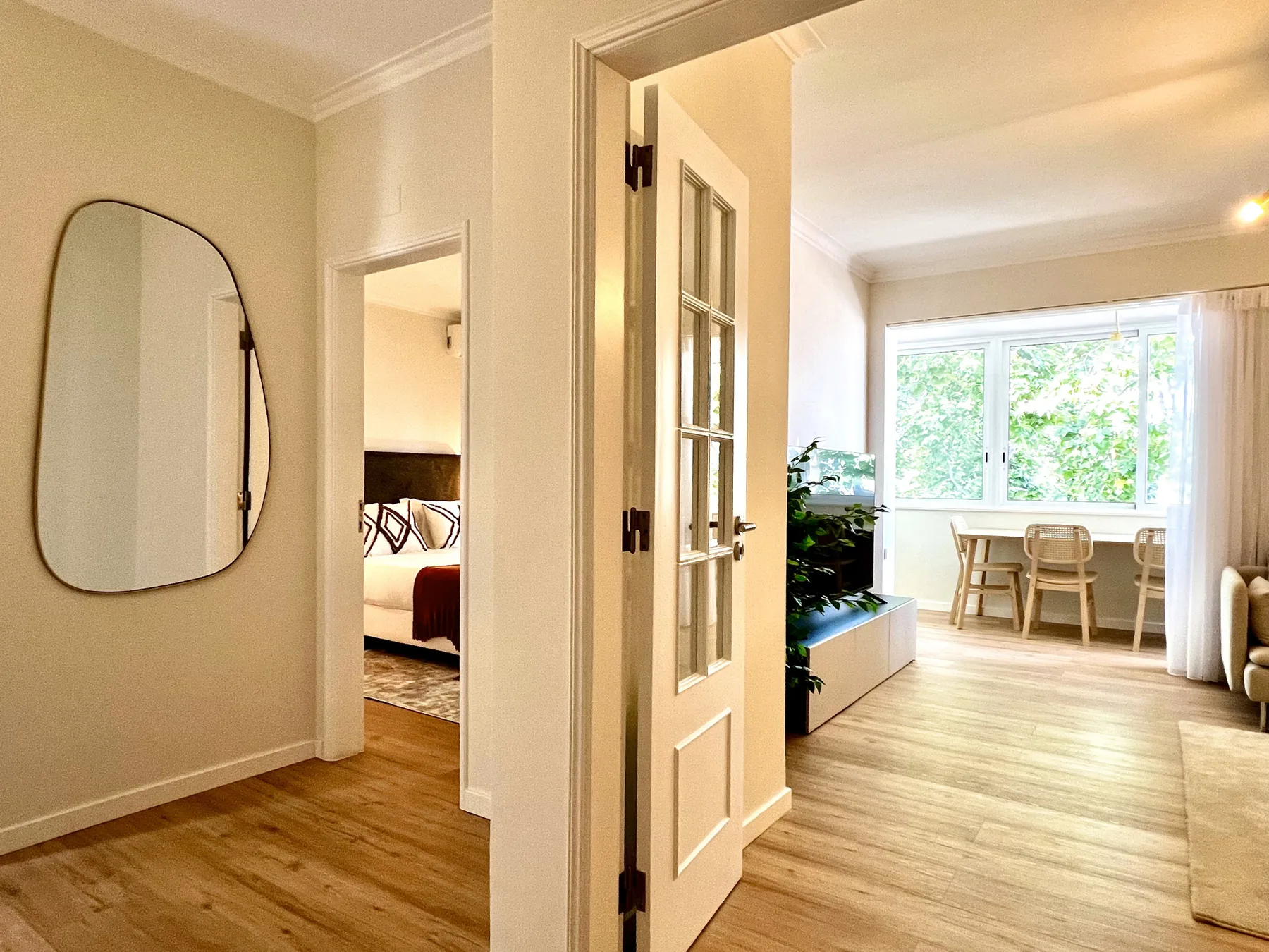 Interior luminoso de un apartamento con una puerta abierta hacia un comedor junto a la ventana.