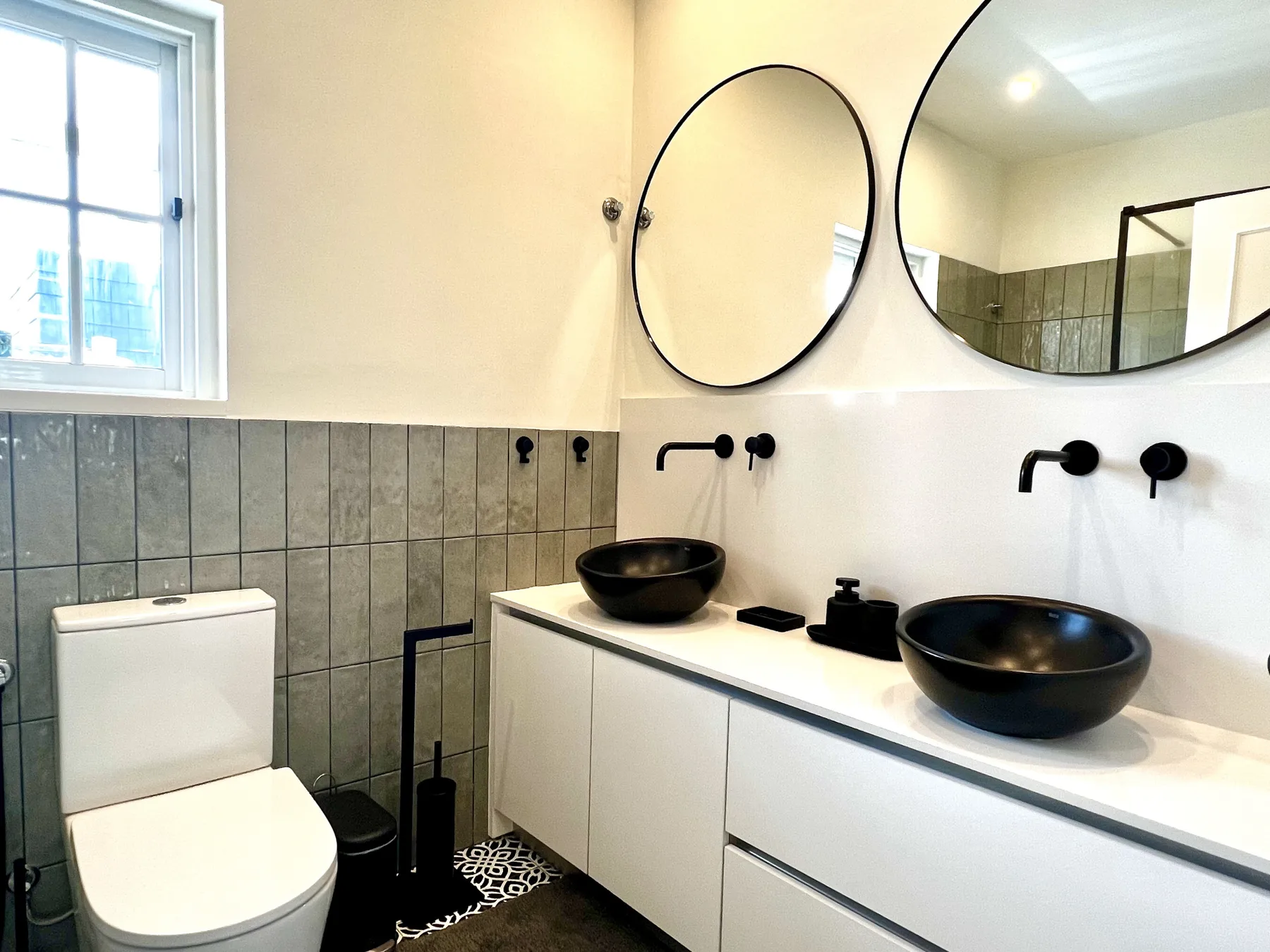 Baño con un lavabo largo, dos lavabos negros sobre encimera y un inodoro.