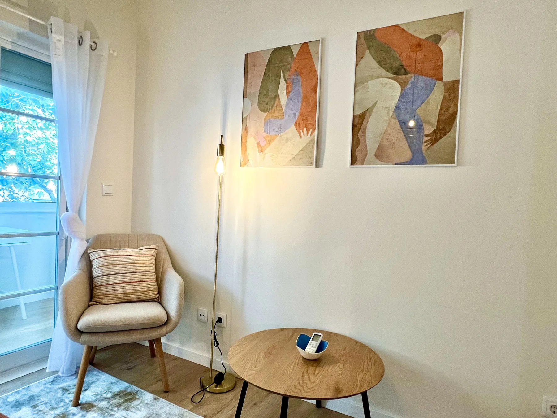 Una pequeña zona de estar con un asiento tapizado, una mesa redonda y arte abstracto en la pared.