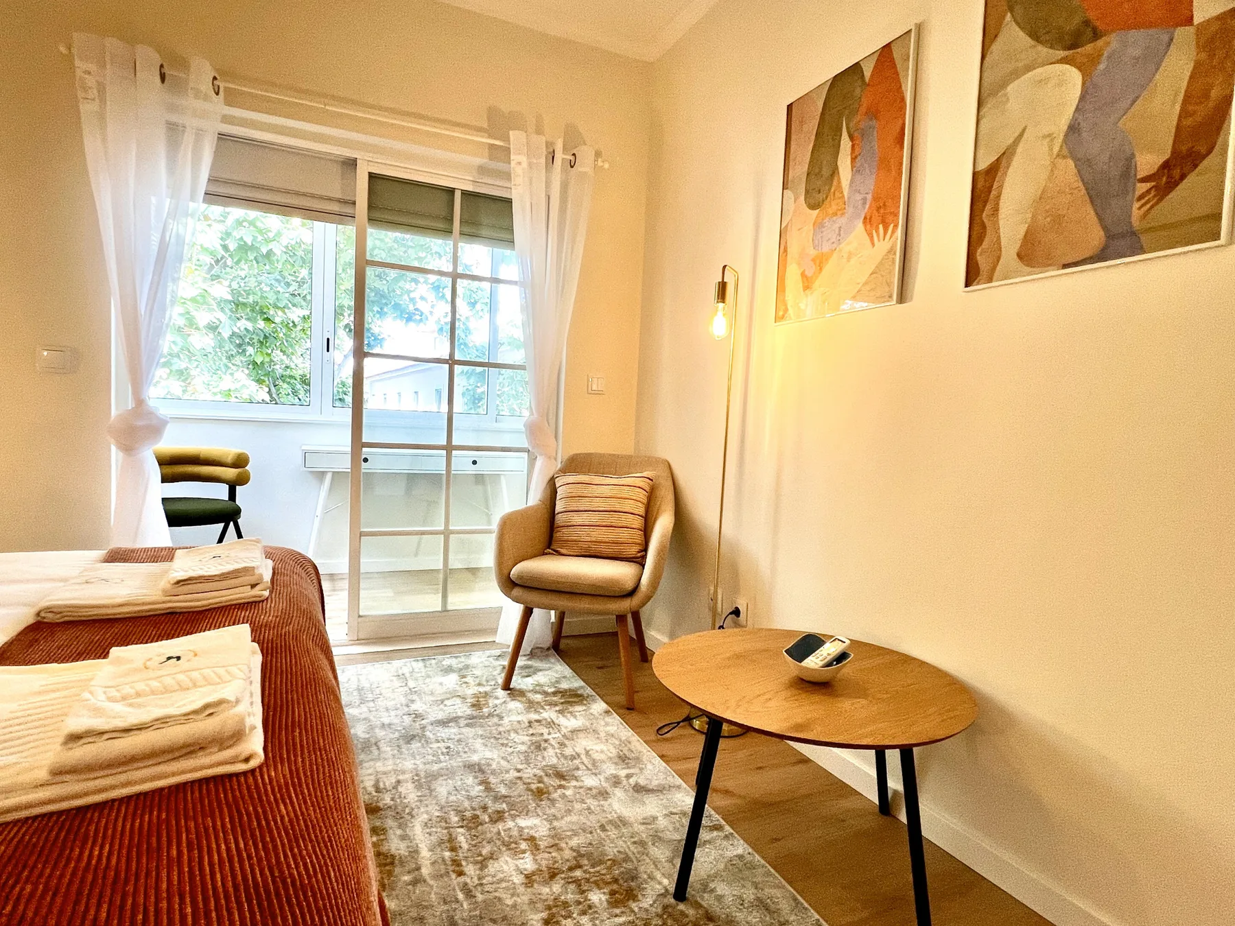 Dormitorio con cama, asientos y una puerta corredera de cristal que da a un balcón.